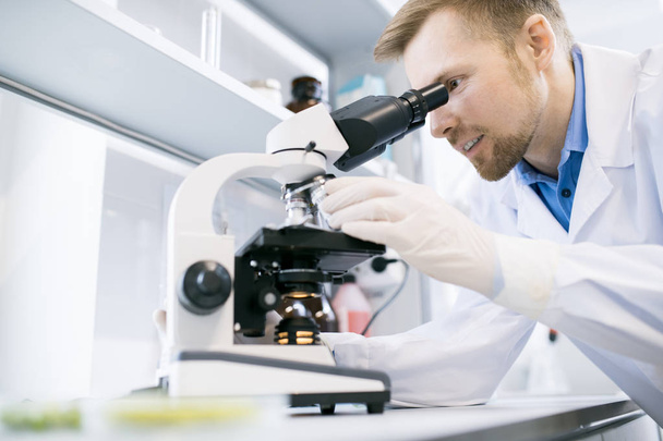 Seitenansicht Porträt eines lächelnden Wissenschaftlers, der im Mikroskop schaut, während er im medizinischen Labor forscht - Foto, Bild