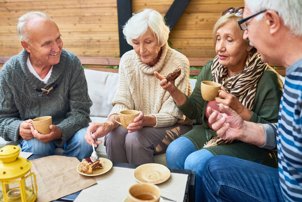 Groep van moderne senioren genieten van tijd samen drinken thee in outdoor cafe en het delen van levensverhalen in pensioen - Foto, afbeelding