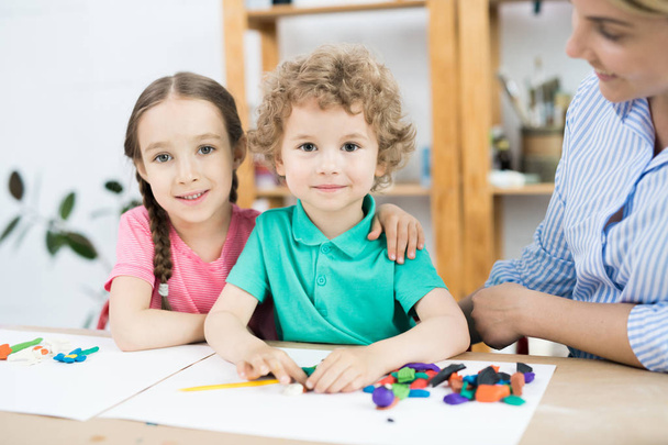 Портрет мальчика и девочки, обнимающихся за столом, сидя на уроке искусства и ремесла
 - Фото, изображение