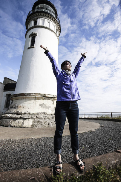 Женщина поднимает руки в радостный момент рядом с маяком Северной головы в Илвако, штат Вашингтон
. - Фото, изображение