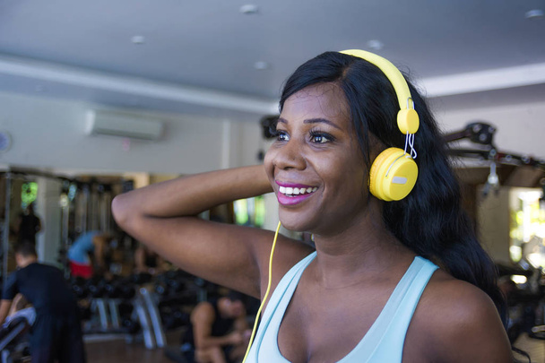 lifestyle indoors portrait at gym of young happy and attractive afro American woman training cheerful at fitness club listening to music with headphones walking on treadmill - Photo, Image