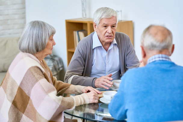 Grupa starszych przyjaciół ciesząc się herbata czas spotkania w domu i udostępniania wspomnień, skupić się na białe włosy starszy mężczyzna rozmowa i gestem - Zdjęcie, obraz