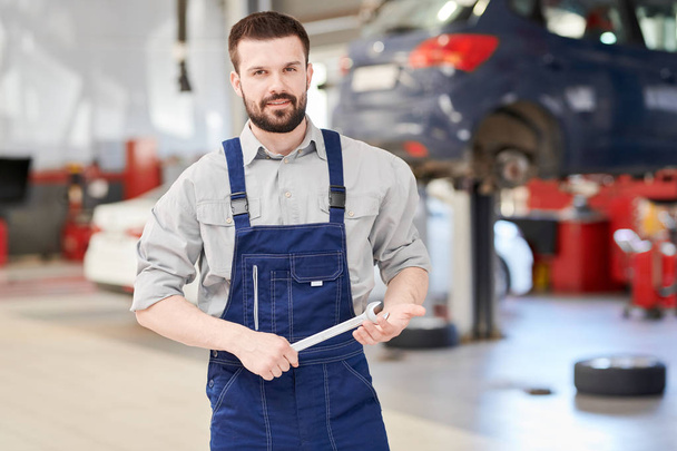 Waist up portrait of modern bearded mechanic holding wrench posing confidently  and smiling at camera while working in car service and repair center, copy space - Foto, Imagem
