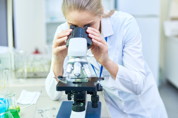 Serious experienced female scientist working with modern microscope while holding scientific research in laboratory - Photo, Image