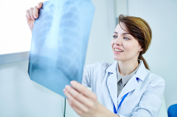 Жінка-лікар тримає рентгенівське зображення грудей, дивлячись на нього і посміхаючись
. - Фото, зображення