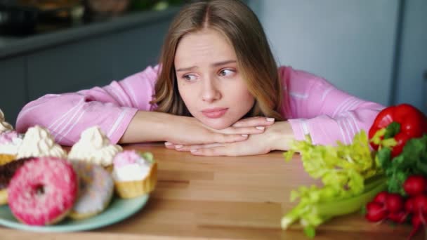 Traurige junge Frau schaut abwechselnd auf gesundes und Junk Food - Filmmaterial, Video