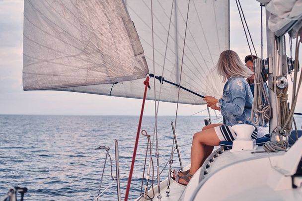 Two female friends relaxing on the yacht with glasses of wine in the hands, during sunset on the high seas. - Foto, Bild