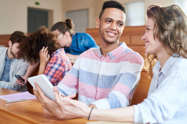 Χαμογελώντας συμμαθητές κάθεται στο γραφείο και στο κολλέγιο η επικοινωνία με άλλα άτομα στο παρασκήνιο - Φωτογραφία, εικόνα