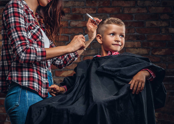 Un bambino in età prescolare sorridente che si taglia i capelli. Bambini parrucchiere con forbici e pettine sta tagliando bambino in camera con interno soppalco
. - Foto, immagini