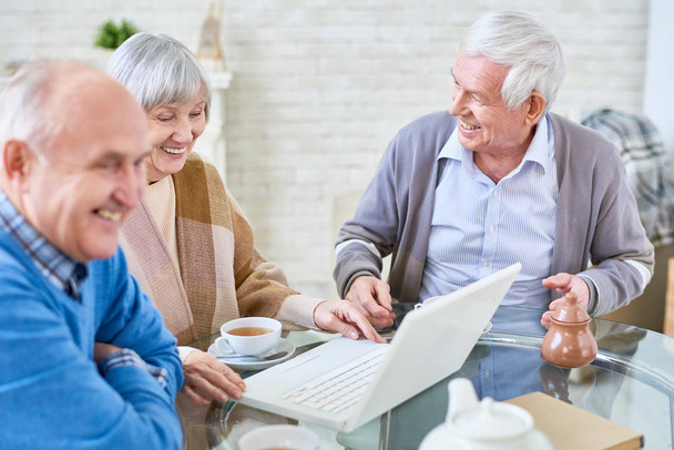 Porträt von drei modernen Senioren mit Laptop im Altersheim und glücklich lächelndem Kopierraum - Foto, Bild