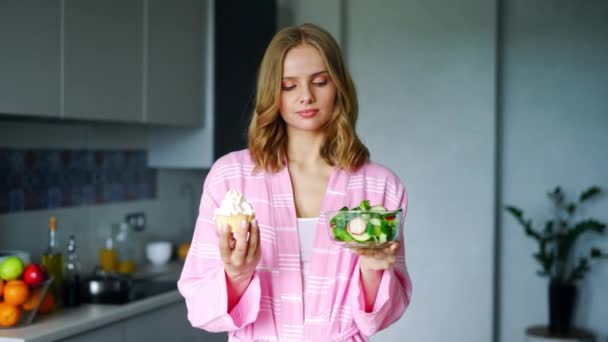 Pretty girl choosing between fresh salad in bowl or cake. Healthy or unhealthy - Metraje, vídeo
