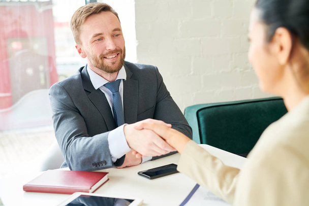 Portrait of handsome business manager shaking hands with female client or partner after successful negotiations during meeting in modern office - Photo, Image
