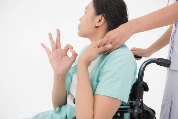 Νοσοκόμα λευκή στολή αγγίξει χέρι και ωθούν μια αναπηρική καρέκλα του ασθενούς πράσινο κοστούμι δείχνουν παλάμη το χέρι της και να εντάξει, σημάδι που απομονώνονται σε λευκό φόντο - Φωτογραφία, εικόνα