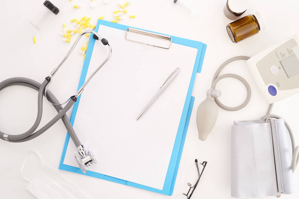 Top view flatlay of doctors tools on white desk composition of stethoscope and  clipboard, glasses and blood pressure monitor, copy space - Photo, Image