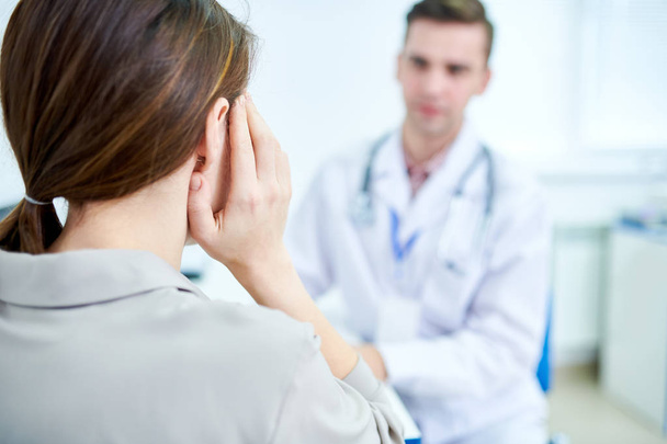 Back view portrait of young woman suffering from headache talking to doctor in clinic, copy space - Photo, Image