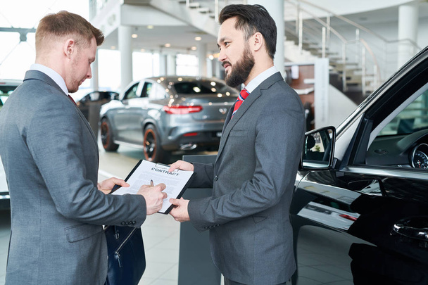 Young man in suit signing a contract for purchase the new car - Fotografie, Obrázek