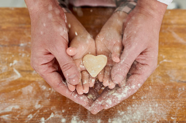 Close up of strong male hands holding tiny childs hands with heart shaped cookie inside, symbol of love, family and bonding - Photo, Image