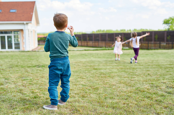 Achteraanzicht portret van kleine jongen spelen met vrienden op groene gazon aan de voorzijde geniet zomer dag in de buitenlucht in de tuin - Foto, afbeelding