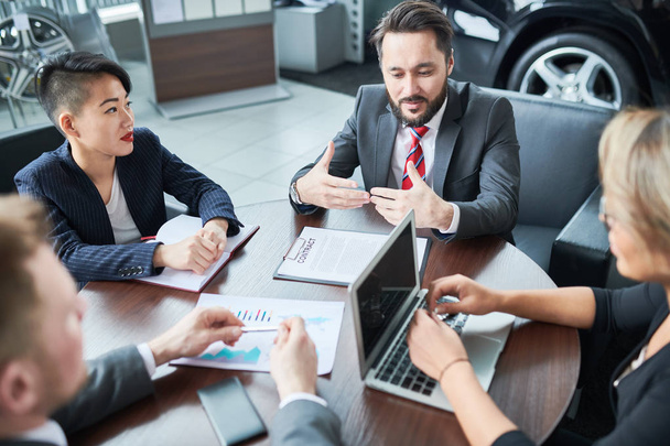 Bearded middle-aged owner of car showroom discussing details of mutually beneficial cooperation with business partners while conducting negotiations - Photo, Image