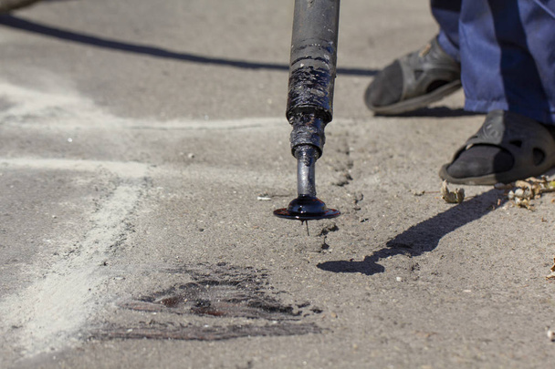 Workers repair the road, pour small cracks with bitumen to prevent further destruction of the road surface. Close up - Zdjęcie, obraz
