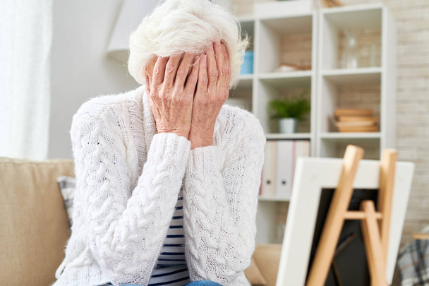 Portrait of depressed senior woman hiding her face and crying while looking at picture of her family, copy space - Photo, Image