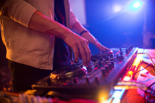 Vista lateral close up de DJ jovem tocando música no clube da moda, foco em mãos sobre misturador DG com luzes iluminadas, espaço de cópia
 - Foto, Imagem
