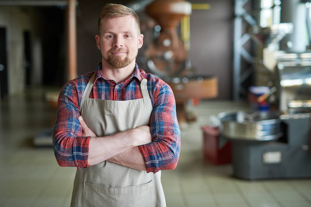 Waist up portrait of modern bearded man wearing apron posing standing confidently with arms crossed against roasting machines in artisan coffee house, copy space - Photo, Image
