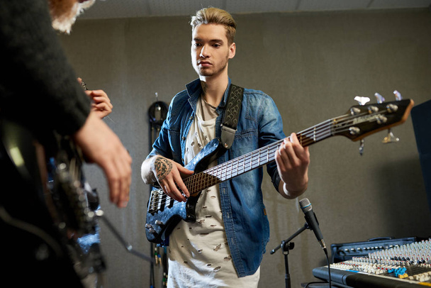 Κομψή άντρες με κιθάρες coworking σε νέο τραγούδι σε σύγχρονο στούντιο ήχου καταγραφή με μικρόφωνα.  - Φωτογραφία, εικόνα