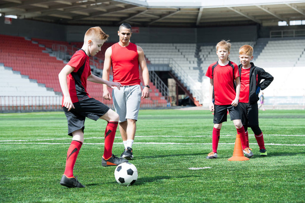 少年サッカー チームの練習、コーチの彼を見ているとボールを前にリードの少年に焦点を当てるの完全な長さの肖像画 - 写真・画像