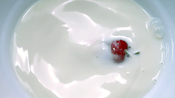Ripe red strawberry falling into a bowl of milk - Materiał filmowy, wideo