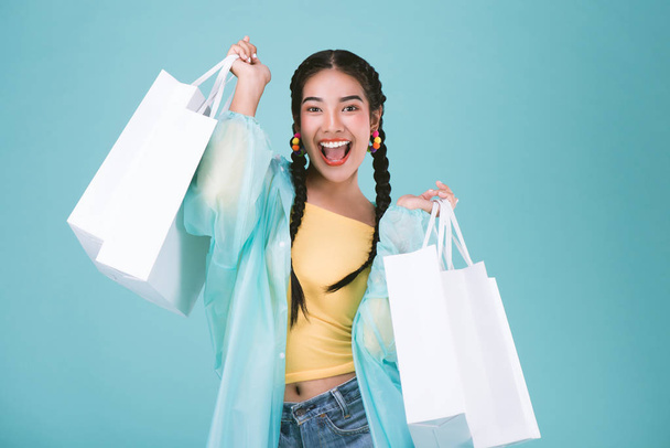 Šťastná mladá žena v pláštěnce s nákupní tašky, Nakupování v deštivý den prodej konceptu, přes modré pozadí. - Fotografie, Obrázek