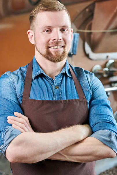 Waist up portrait of modern bearded man wearing apron posing standing confidently with arms crossed against roasting machines in artisan coffee house - Fotoğraf, Görsel