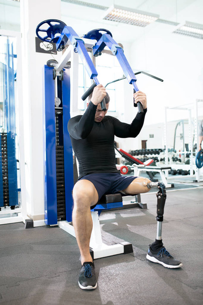 Protez bacak modern spor salonunda makinasıyla ağırlıkları ile çalışma dışarı ile yakışıklı kaslı adam portresi tam uzunlukta - Fotoğraf, Görsel