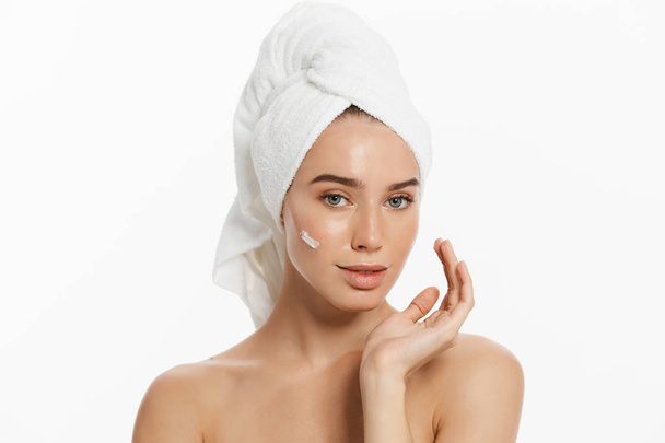 Close up beauty portrait of a smiling beautiful half naked woman with towel on her hair applying face cream isolated over white background. - Foto, Imagen