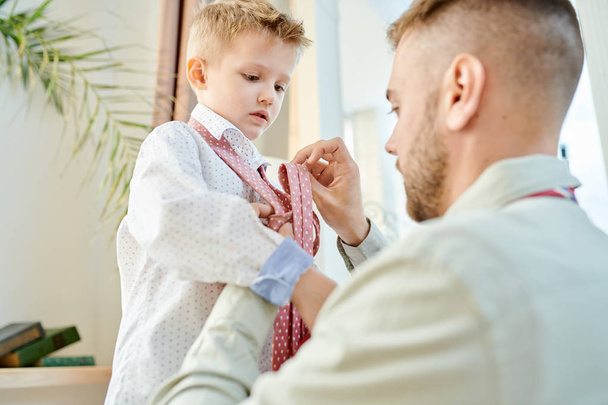 A jóvágású apja segít az aranyos kis fia nyakkendő nyakkendő a családi vacsora meleg tónusú portré - Fotó, kép