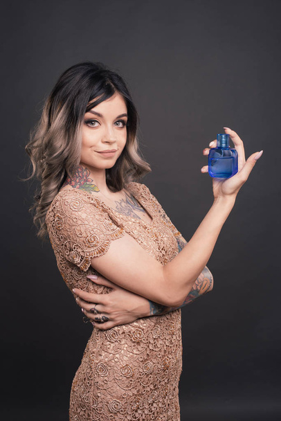 Elegant sensual young woman holding perfume. Fashion photo of young magnificent Girl . Studio photo. Perfect Skin. Professional Make-up. Makeup. Fashion Art. Vogue Style. Color tattoo - 写真・画像