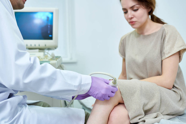 Ernteunschärfe Ansicht des medizinischen Spezialisten Überprüfung Knie der schönen Frau durch Gerät - Foto, Bild