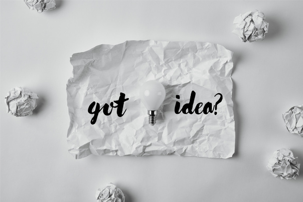 bovenaanzicht van energiebesparende lamp op verfrommeld papier met inspiratie "got idee?" - Foto, afbeelding