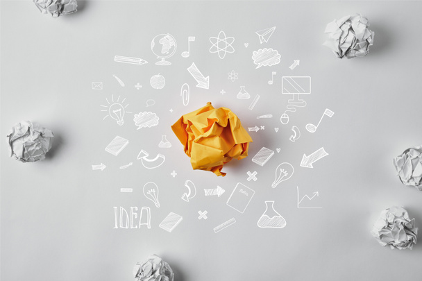 top view of crumpled yellow paper surrounded with business idea icons and white crumpled papers on white surface - Foto, imagen
