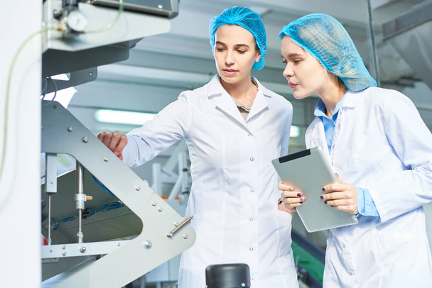 Ritratto di due giovani donne che indossano camici che lavorano in una moderna fabbrica alimentare e sorridono mentre controllano il processo di produzione in piedi accanto alle unità elettriche in officina, copiare lo spazio
 - Foto, immagini