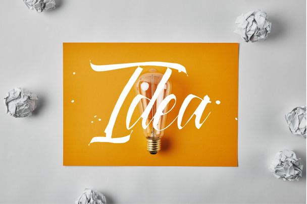 Idea concept with top view of incandescent lamp on blank yellow paper surrounded with crumpled papers  - Photo, Image