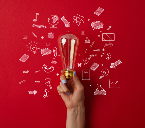 cropped shot of woman holding vintage incandescent lamp with business icons on red surface - Photo, Image