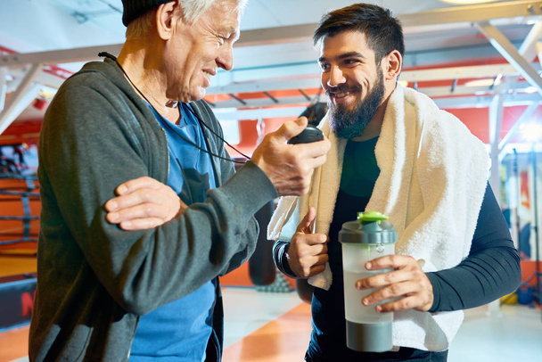 Cheerful elderly coach and bearded man taking rest after workout and chatting happily.  - Foto, Imagen