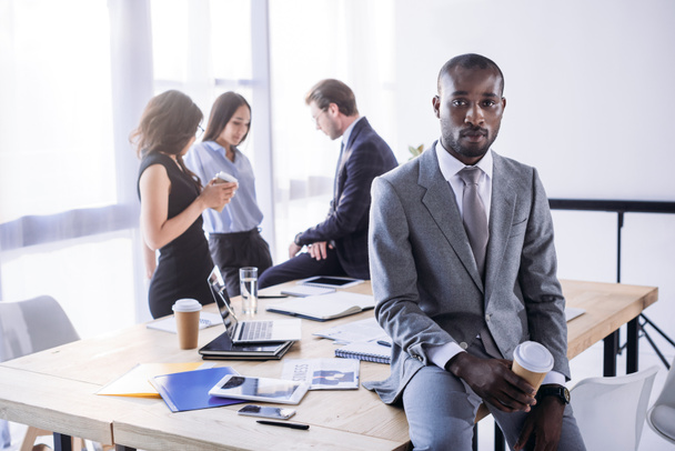 вибірковий фокус афроамериканського бізнесмена з кавою, щоб піти і колег на робочому місці в офісі
 - Фото, зображення
