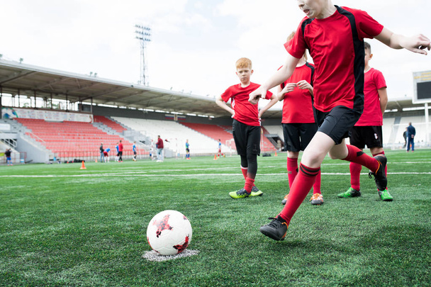 Action shot of  teenage boy forcefully kicking ball during football match on outdoor stadium, copy space - Valokuva, kuva