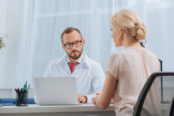fizyoterapist beyaz ceket konuşmayı bayan hasta ile hastane içinde laptop ile işyerinde - Fotoğraf, Görsel