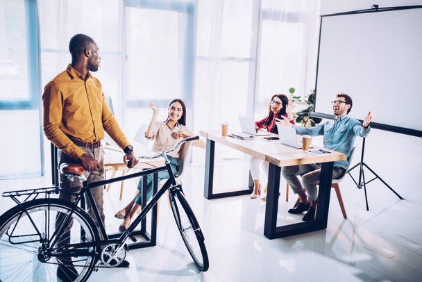 multicultural business people greeting african american colleague with bicycle in office - Foto, Bild