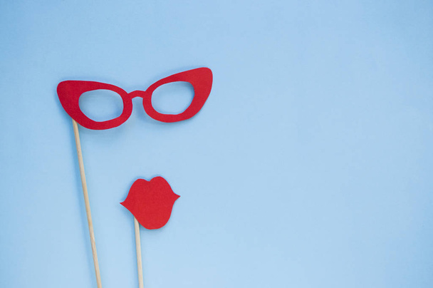 Rojo brillante cabina de fotos gafas de utilería y labios sobre fondo azul con copyspace
. - Foto, imagen