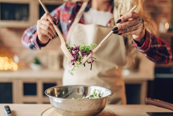 Huisvrouw in schort koken van verse salade, keuken interieur op de achtergrond. Gelukkig vrouwelijke kok. Voedselbereiding door chef-kok - Foto, afbeelding