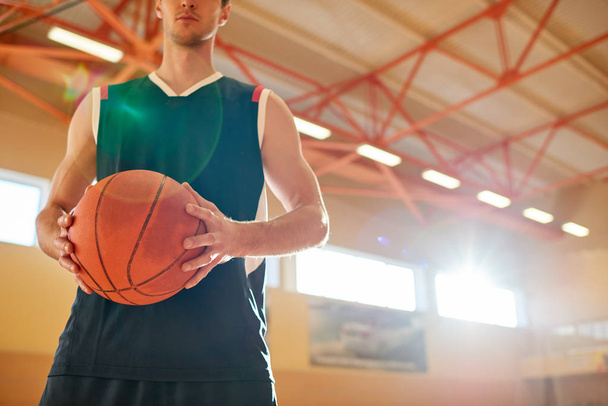 Crop man en basket-ball vêtements de sport tenant le ballon tout en se tenant sur le terrain dans la salle de gym
.  - Photo, image